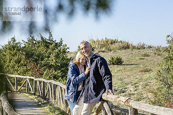 Lächelndes Paar umarmt sich an einer Holzbrücke