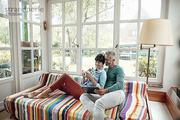 Mann teilt Tablet-PC mit Frau  die Kaffeetasse auf dem Sofa hält