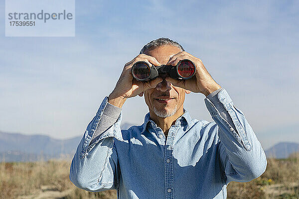 Man looking through binoculars on sunny day