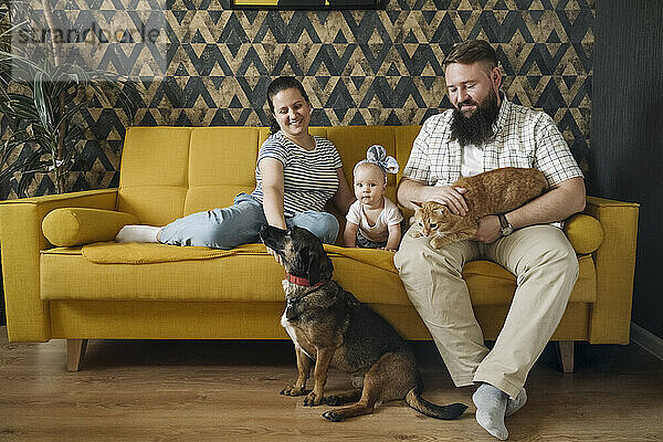 Lächelnde Familie mit kleinem Mädchen und Haustieren im Wohnzimmer
