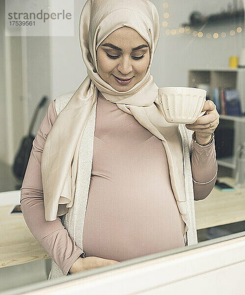 Schwangere Frau mit Kaffeetasse durch Fenster gesehen