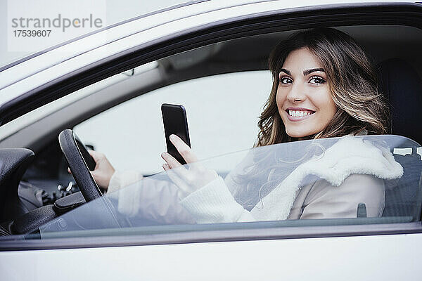 Lächelnde Frau hält Smartphone im Auto