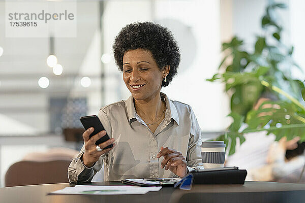 Lächelnde Geschäftsfrau benutzt Smartphone im Büro