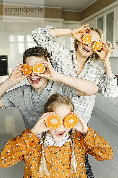 Playful family covering eyes with slices of oranges at home