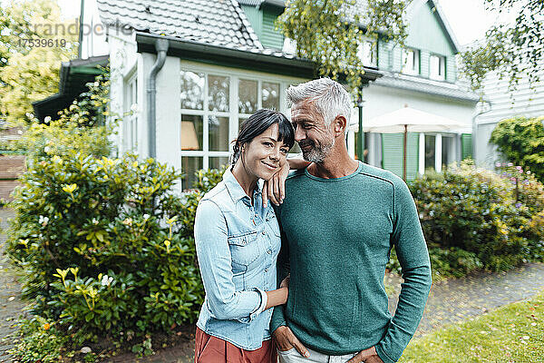 Smiling mature man looking at woman standing with hand on shoulder in backyard