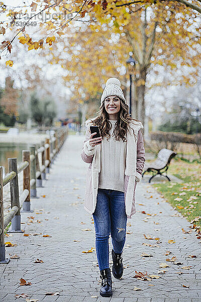 Junge Frau mit Handy geht im Herbstpark spazieren