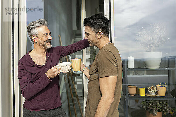 Gay men toasting coffee cups at balcony