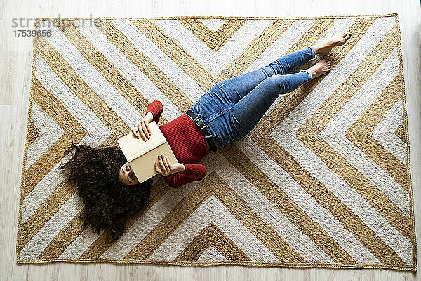 Woman with book lying on carpet at home