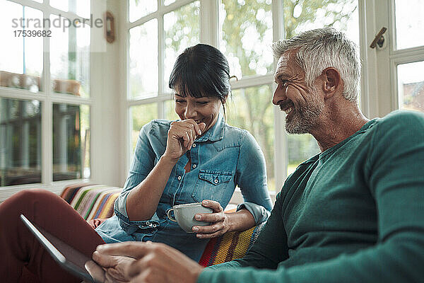 Lächelnder Mann unterhält sich mit Frau  die zu Hause eine Kaffeetasse hält