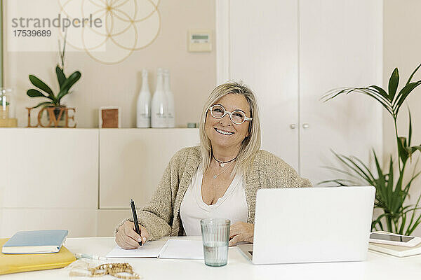 Smiling businesswoman with laptop on desk at office