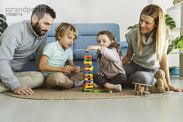 Eltern schauen Sohn und Tochter beim Jenga-Spielen im Wohnzimmer zu