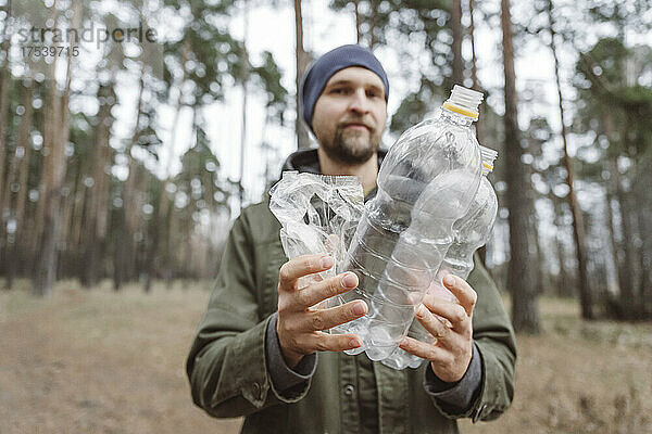 Mann hält Plastikwasserflaschen im Wald