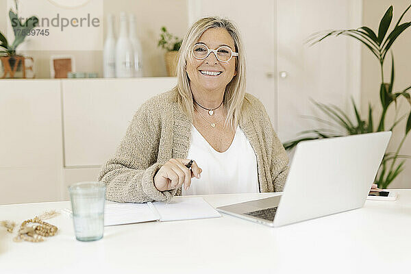 Smiling businesswoman with laptop on desk at workplace