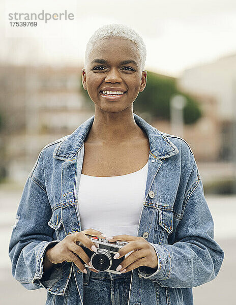 Lächelnde Frau in Jeansjacke mit alter Kamera