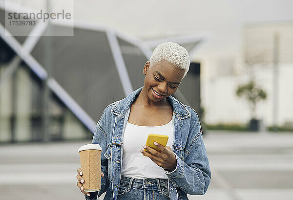 Lächelnde Frau benutzt Smartphone und hält Einwegbecher in der Hand