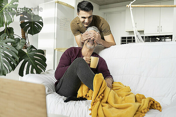 Smiling man covering husband's eyes with hands at home