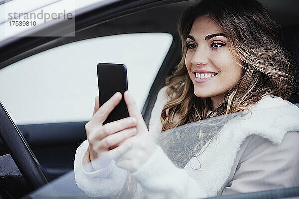 Smiling woman using mobile phone in car
