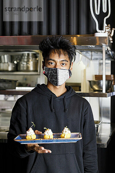Waiter with protective face mask holding dessert tray in restaurant