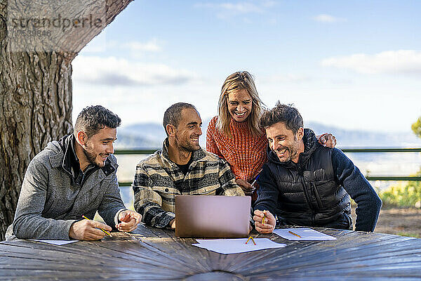 Cheerful man using laptop sitting with friends at table