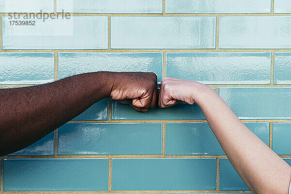 Man and woman giving fist bump on turquoise brick wall