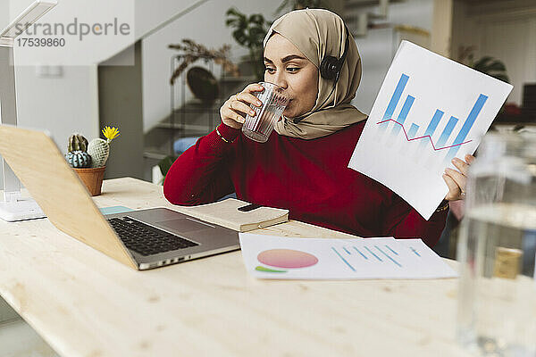 Geschäftsfrau trinkt Wasser und arbeitet zu Hause am Laptop