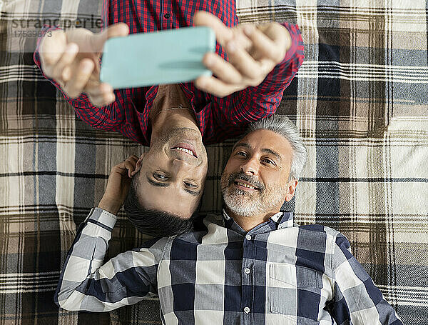 Smiling gay couple taking selfie through smart phone at home