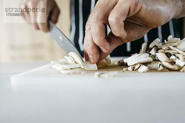 Mann schneidet zu Hause Pilze mit Küchenmesser auf Schneidebrett