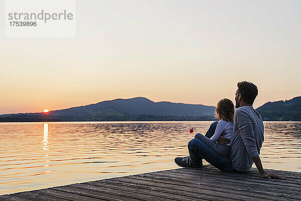 Vater und Tochter betrachten den Sonnenuntergang vom Steg aus  Mondsee  Österreich