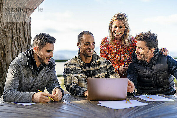 Happy man using laptop discussing with friends sitting at table