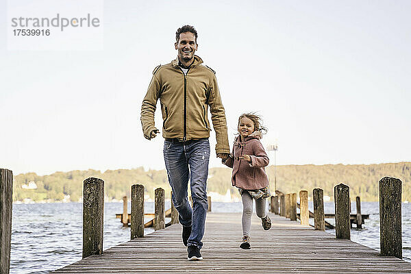 Smiling father holding hand of daughter and running on jetty