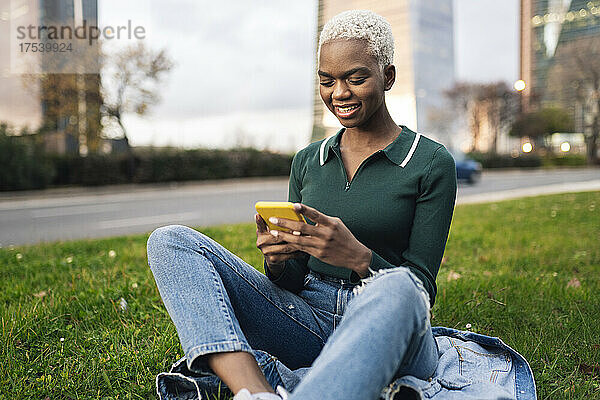 Junge Frau sitzt mit Smartphone im Gras am Straßenrand