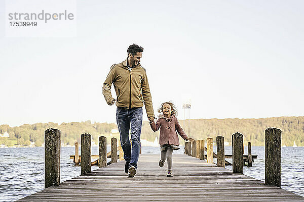 Fröhlicher Mann und Mädchen laufen gemeinsam auf dem Steg