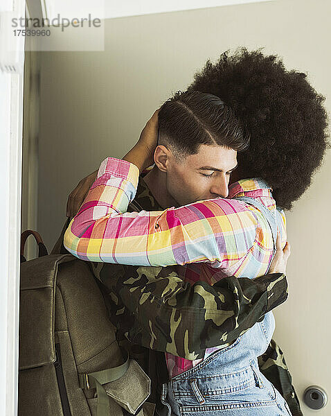 Young woman welcoming and embracing soldier man at doorway