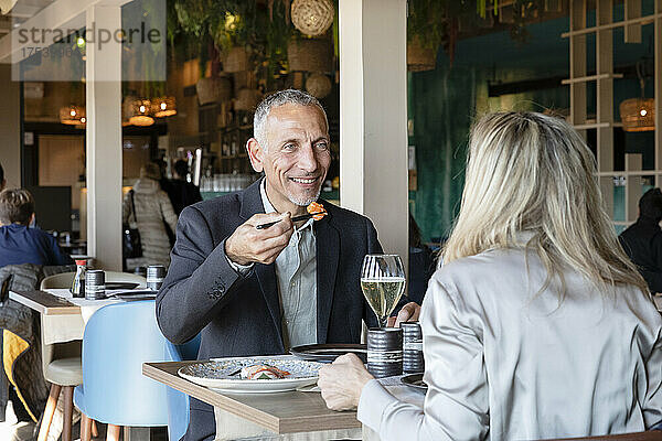Smiling man holding sushi looking at woman in restaurant