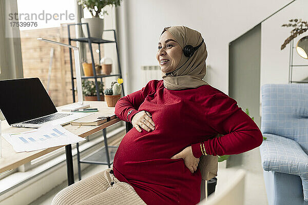 Lächelnde schwangere Geschäftsfrau  die zu Hause freiberuflich arbeitet