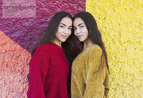 Smiling sisters standing by multi colored wall