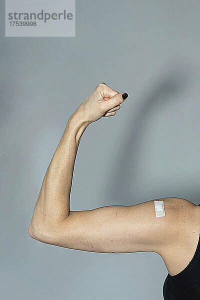 Woman with bandage flexing muscle over gray background