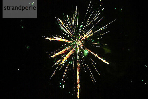 Green and yellow fireworks exploding against clear night sky