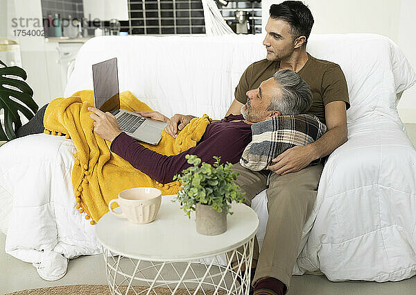 Gay couple using laptop on sofa in living room