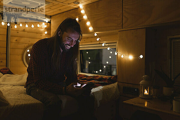 Smiling man using smart phone in illuminated van