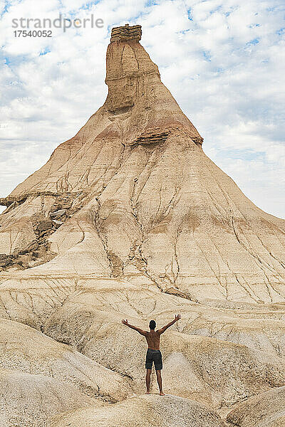 Man standing with arms outstretched in front of eroded mountain  Bardenas Reales  Navarra  Spain