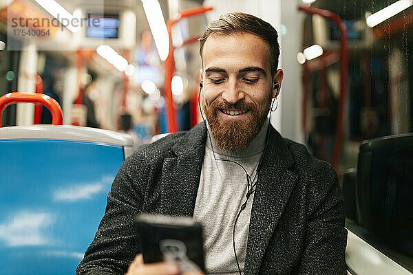 Happy bearded man using mobile phone and listening music through in-ear headphones