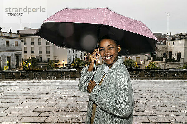 Happy girl with umbrella standing on footpath