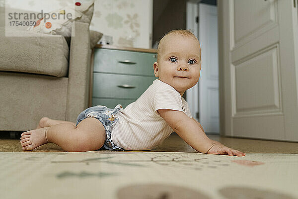 Smiling baby girl lying on floor at home