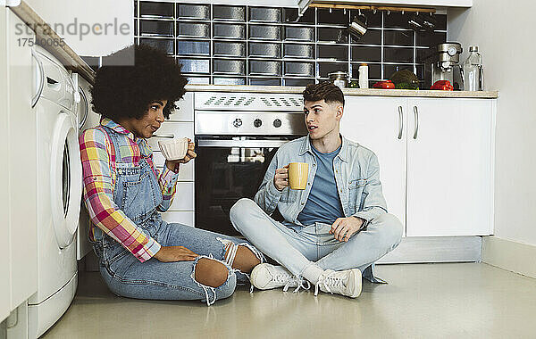 Multiracial couple having coffee together sitting in kitchen at home