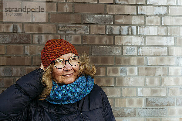 Senior woman adjusting knit hat in front of wall
