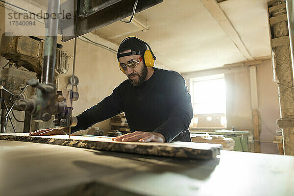 Holzarbeiter sägt Holz mit einer Bandsäge in der Werkstatt