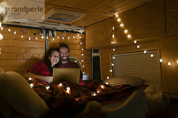 Happy couple watching movie on laptop in illuminated motor home