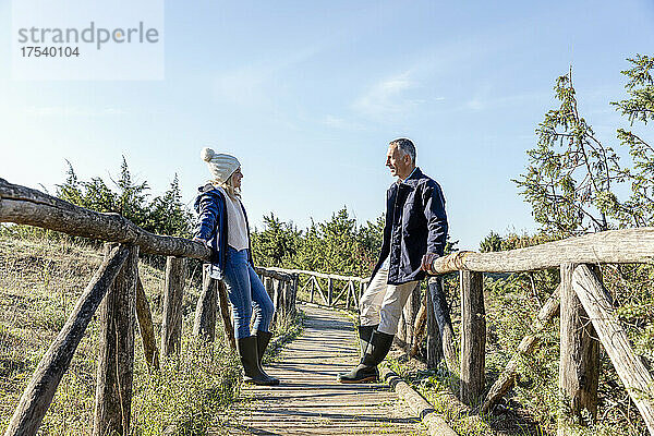 Mann und Frau schauen einander an und lehnen sich an eine Holzbrücke