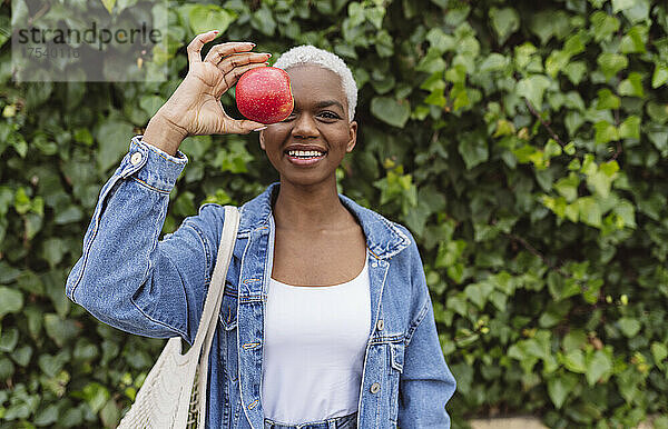 Frau  die vor der Pflanze steht und ihr Auge mit einem Apfel bedeckt